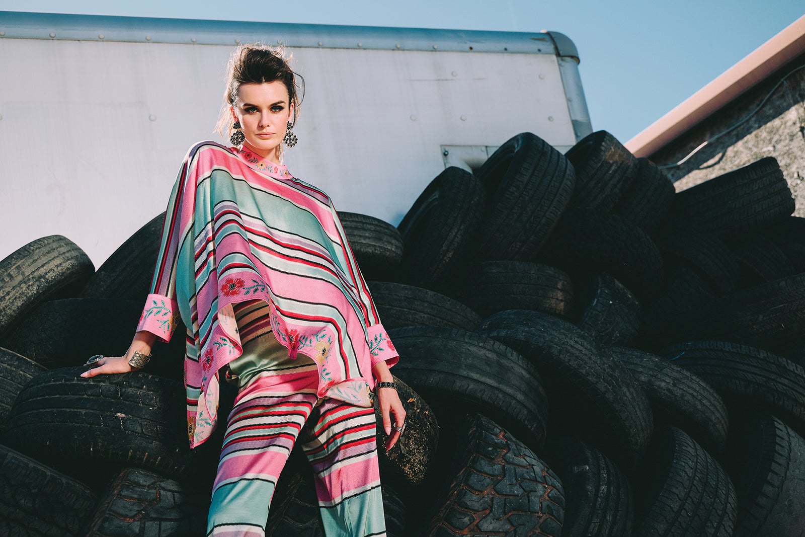 Kaylin wearing the Round Top Serape Poncho and Pants posed in front of a stack of used tires.
